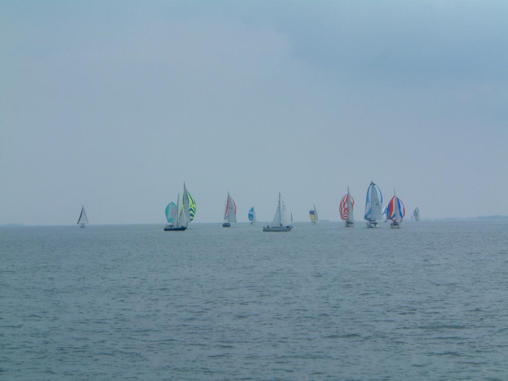 Several sailboats with colorful sails move across the open water under a cloudy sky.