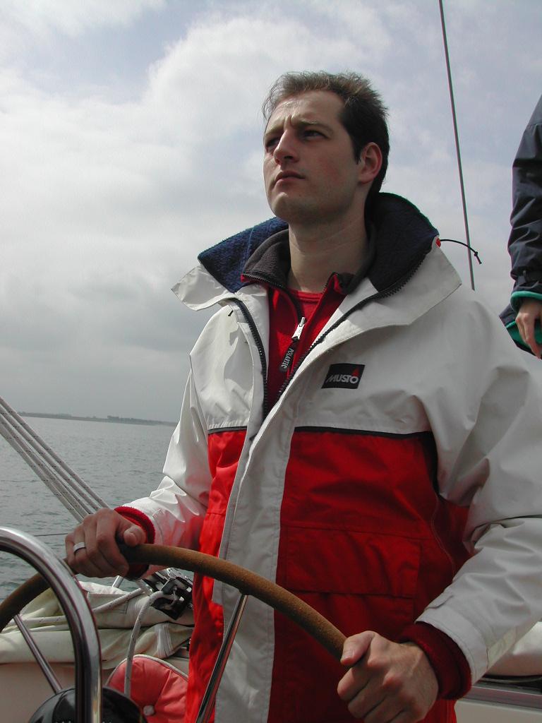 A person in a red and white jacket steers a boat, looking ahead with a focused expression.