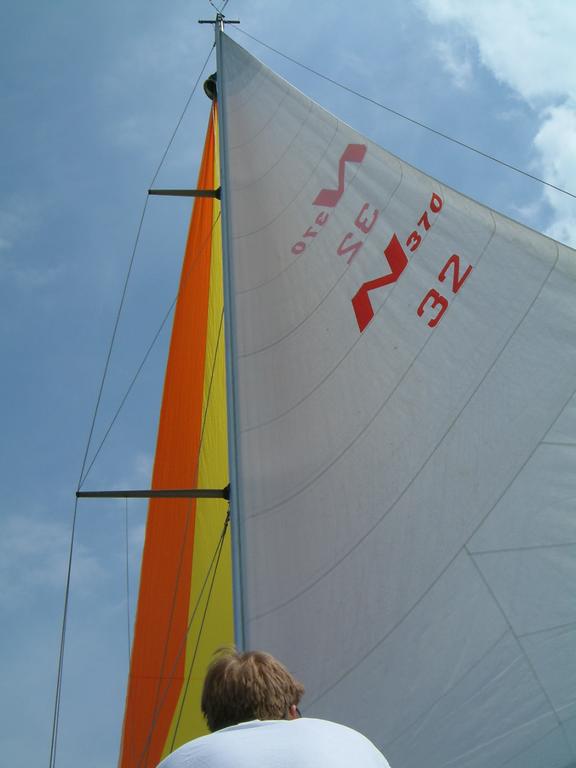 A person looks up at the large sail of a boat against a partly cloudy sky.