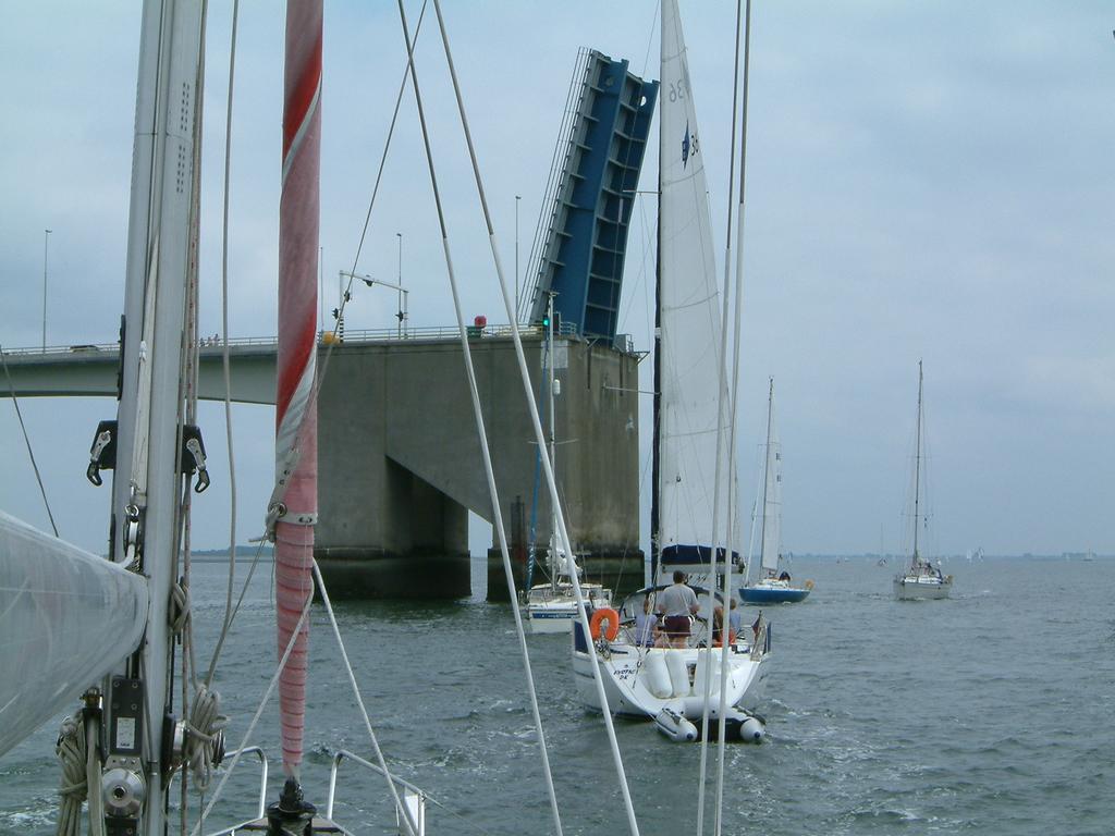 Several sailboats approach a raised drawbridge over the water, allowing them to pass through.