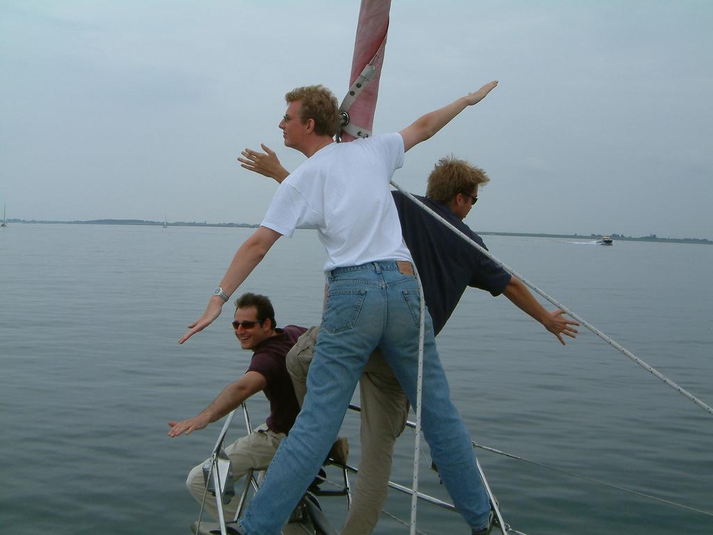 Three people stand at the bow of a boat, extending their arms in a "Titanic" movie pose over the water.