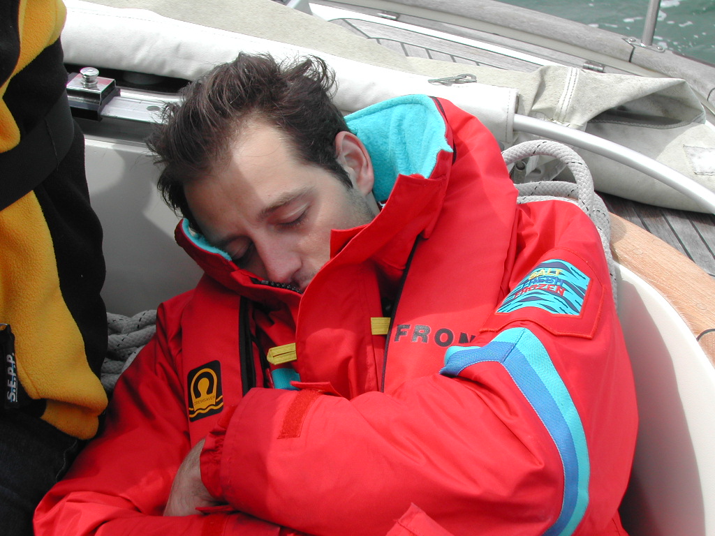A person in a red jacket is sleeping on a boat, leaning against the side with arms crossed.
