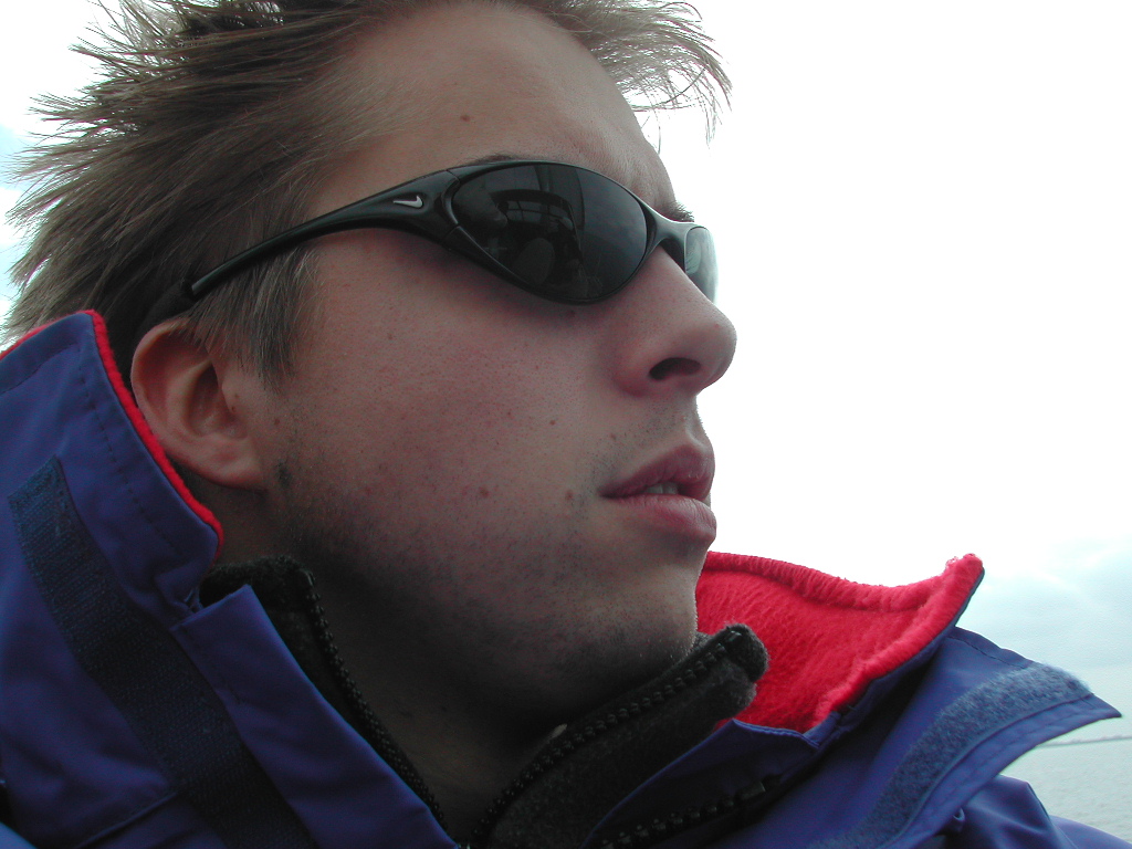 A person wearing sunglasses and a jacket looks into the distance with a neutral expression.
