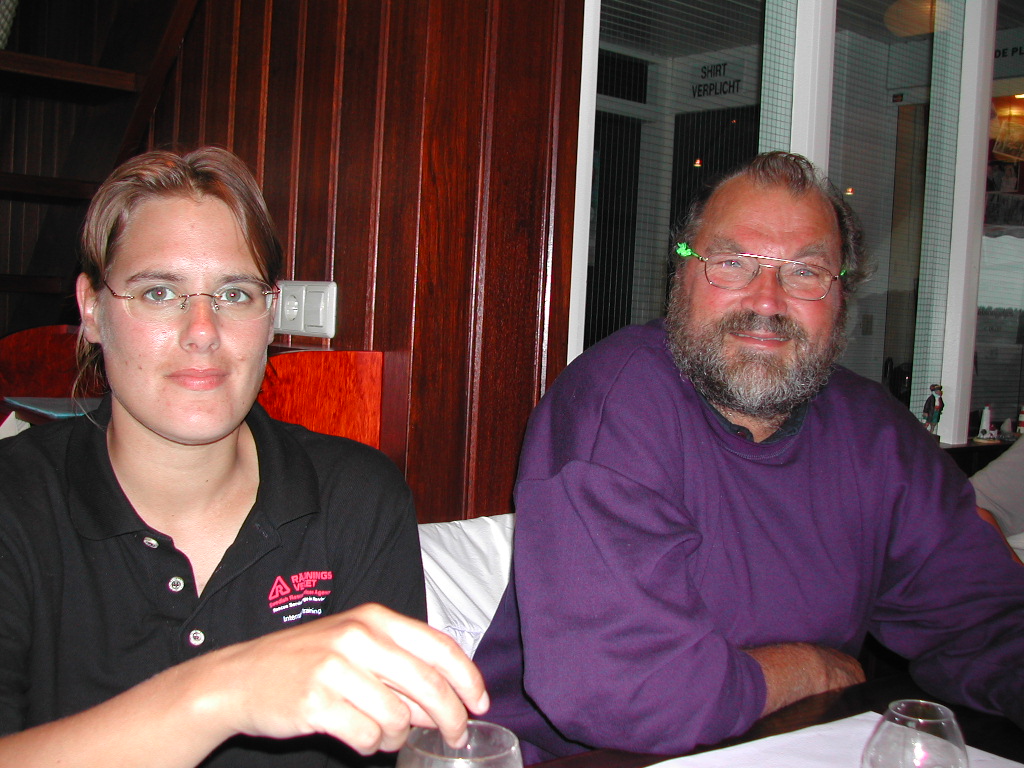A woman and a man sit at a table indoors, both wearing glasses.