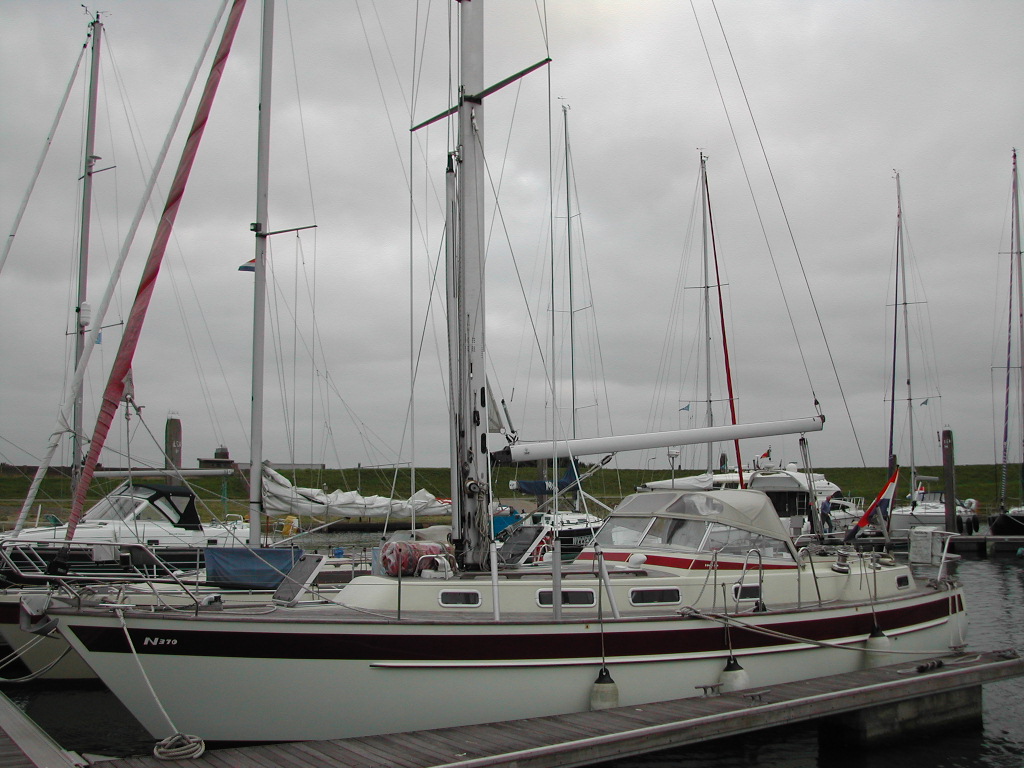 A sailboat with a white and red hull is docked at a marina, surrounded by other boats and masts.