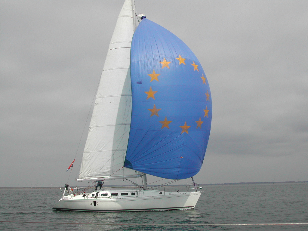 A white sailboat moves through the water with a large blue sail featuring yellow stars.