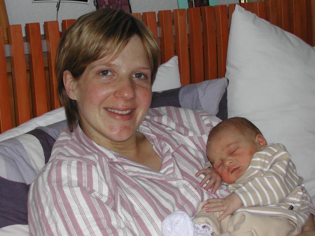 A woman in striped pajamas smiles while holding a sleeping newborn baby dressed in striped clothing.