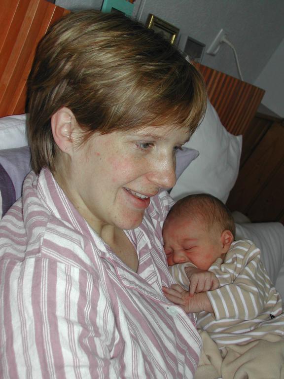 A woman in striped pajamas smiles while holding a sleeping newborn baby dressed in striped clothing.