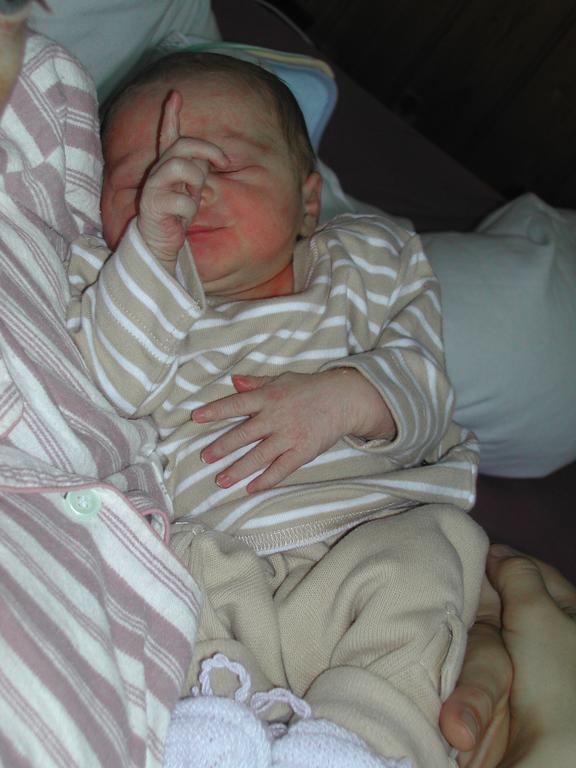 A newborn baby in striped clothing is being held, with one hand near their face and eyes partially closed.