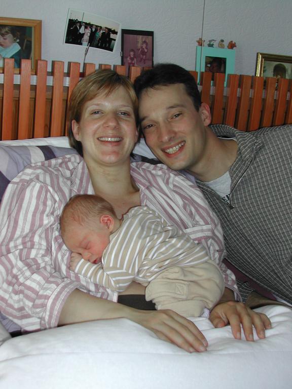A smiling couple sits together while the mother holds a sleeping newborn baby on her chest.