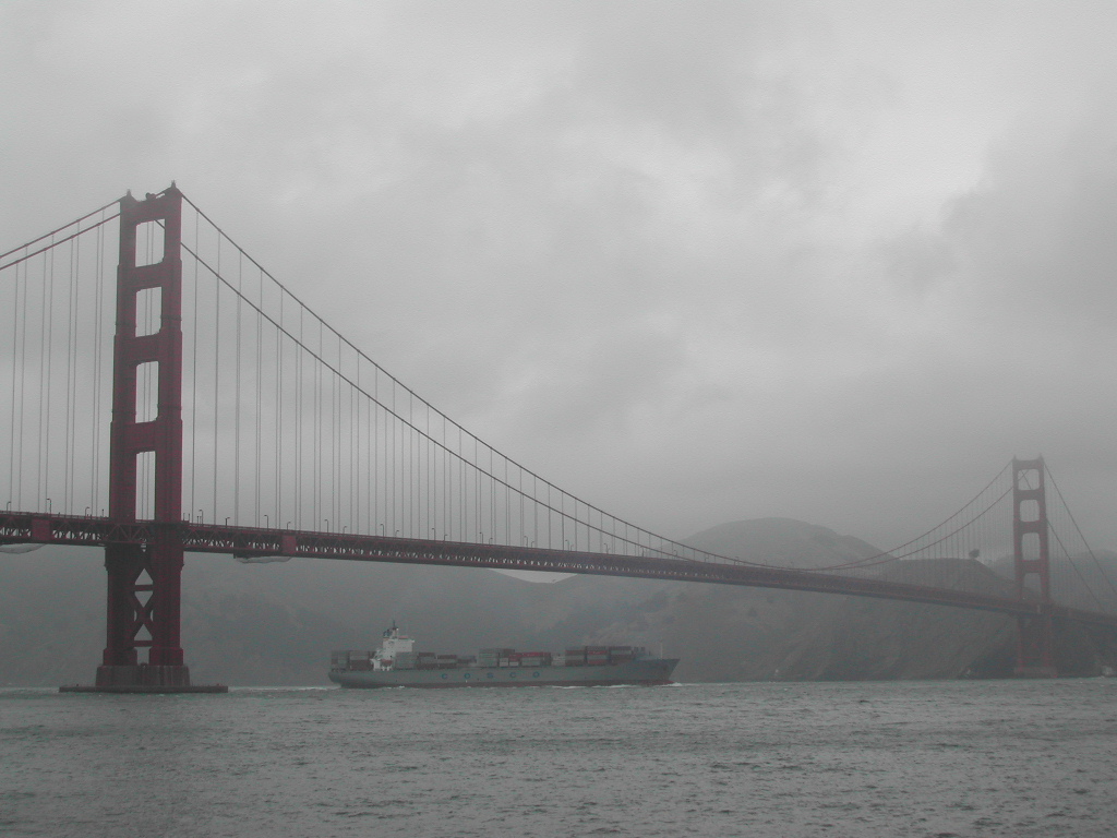 A large cargo ship passes under the Golden Gate Bridge on a cloudy day.