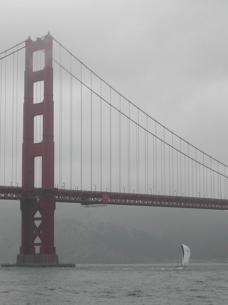 The Golden Gate Bridge on a foggy day with a sailboat passing underneath on the water.