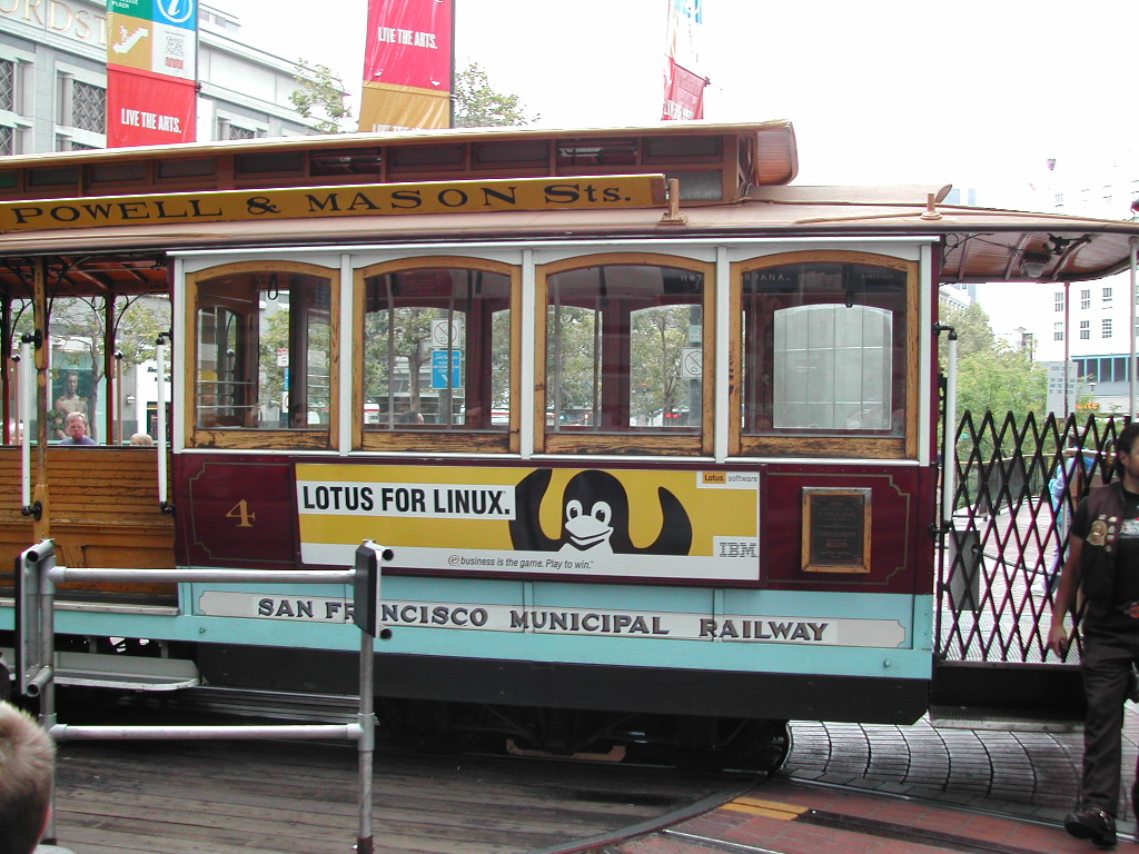 A San Francisco cable car with a "Lotus for Linux" advertisement featuring the Linux penguin mascot on its side.
