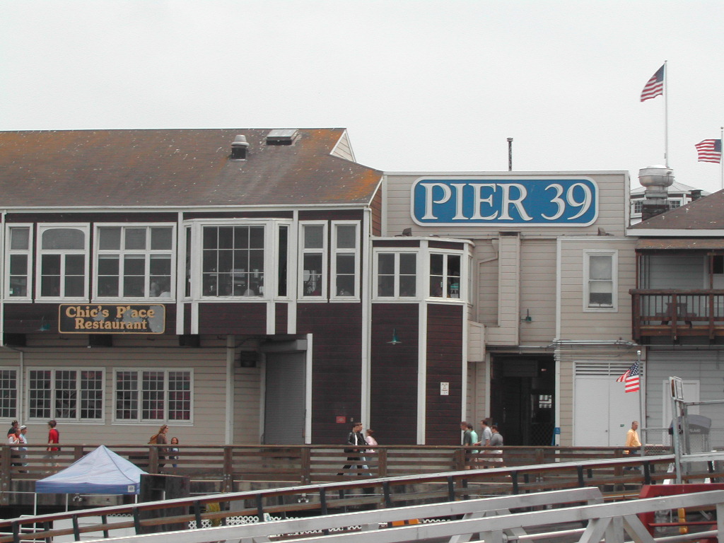 A view of Pier 39 in San Francisco, showing buildings, a restaurant sign, and people walking along the pier.