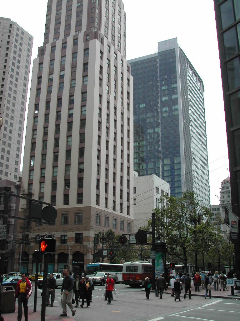 Busy city intersection in San Francisco with pedestrians crossing, buses, cars, and tall buildings in the background.
