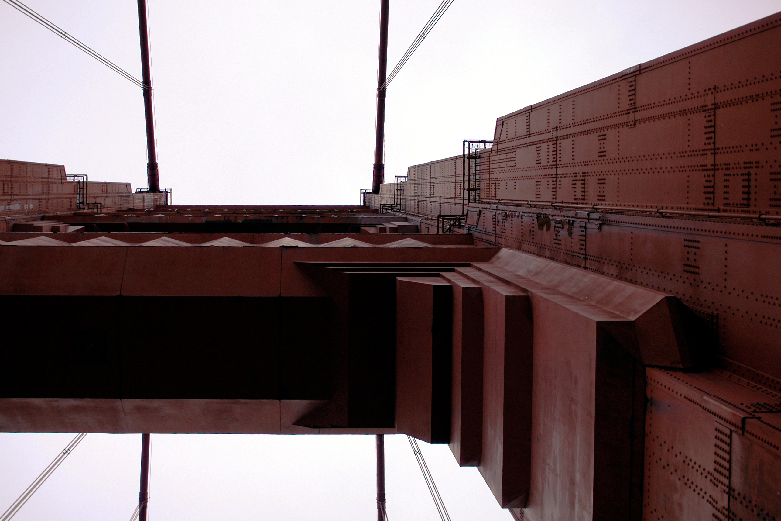 Low-angle view of the Golden Gate Bridge, showing its steel structure, rivets, and suspension cables against the sky.