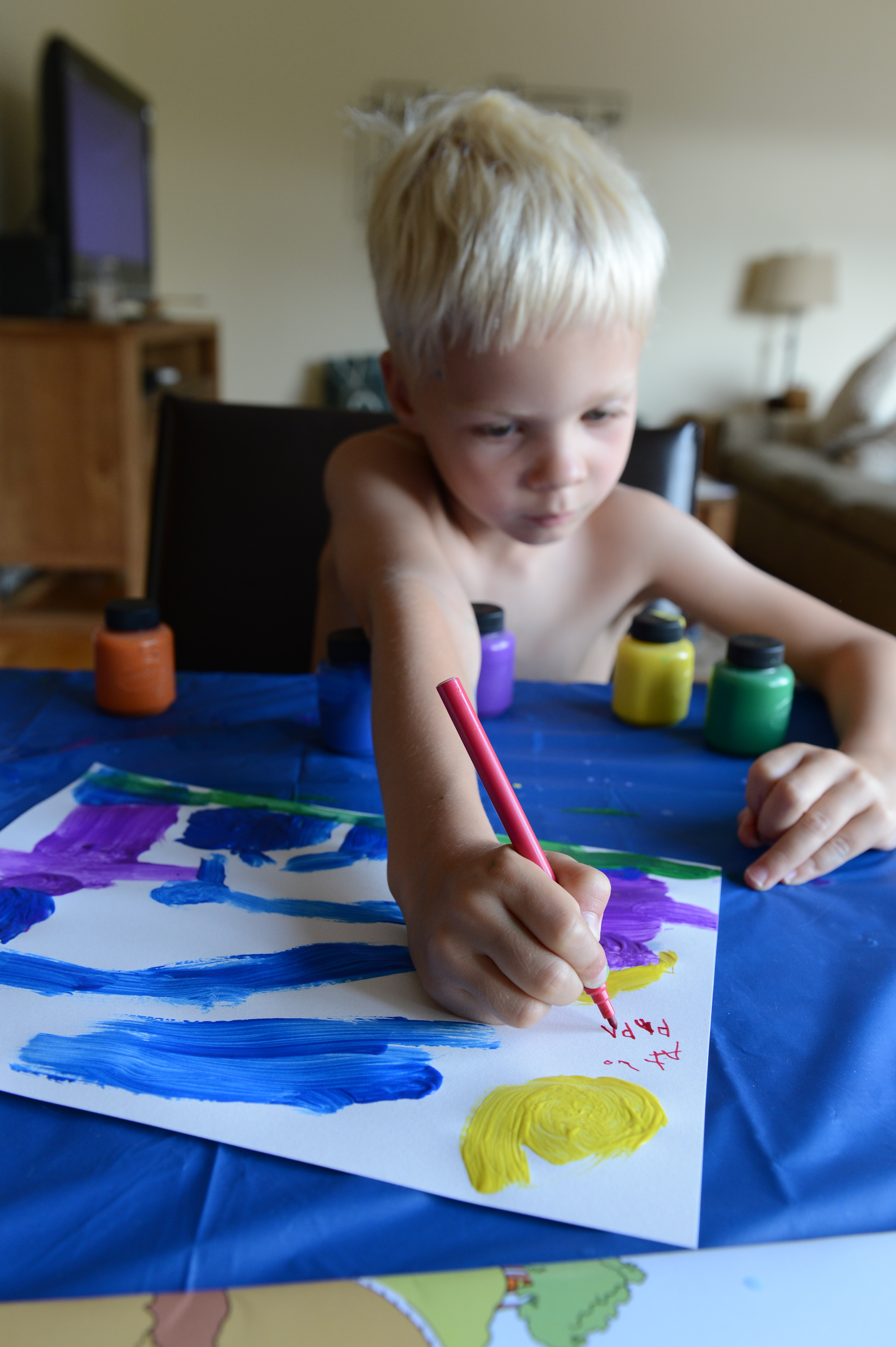 A young child paints on paper with bright colors, holding a red pencil and focusing on their artwork.