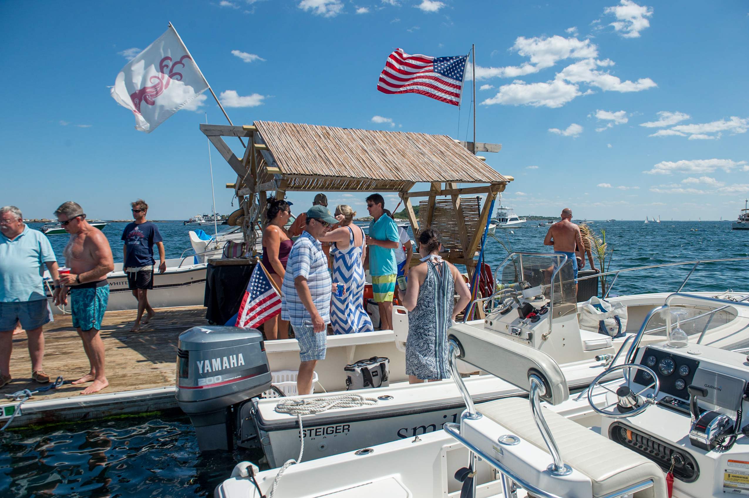 A group of people gathers on a dock, chatting and preparing to board boats on a sunny day.