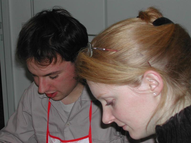 A man wearing an apron and a woman are closely looking down at something during a meal or preparation.