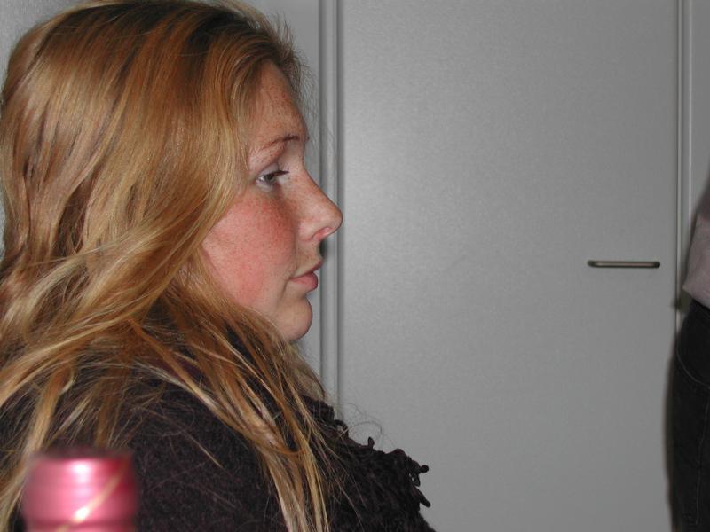 A woman with long blonde hair sits at a table, looking to the side during a gathering.