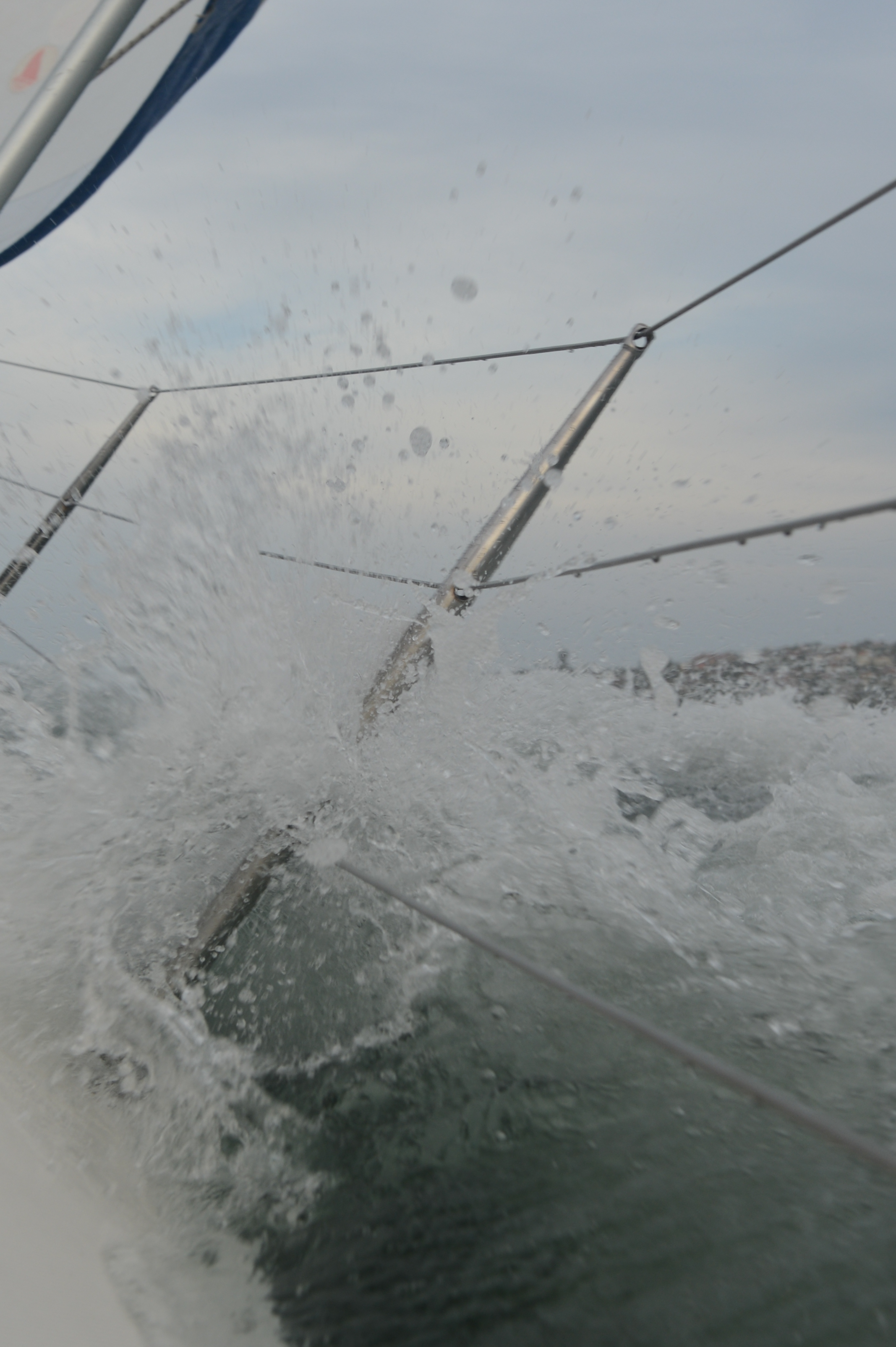 Water splashes against the metal railing of a sailboat, with taut ropes stretching diagonally.
