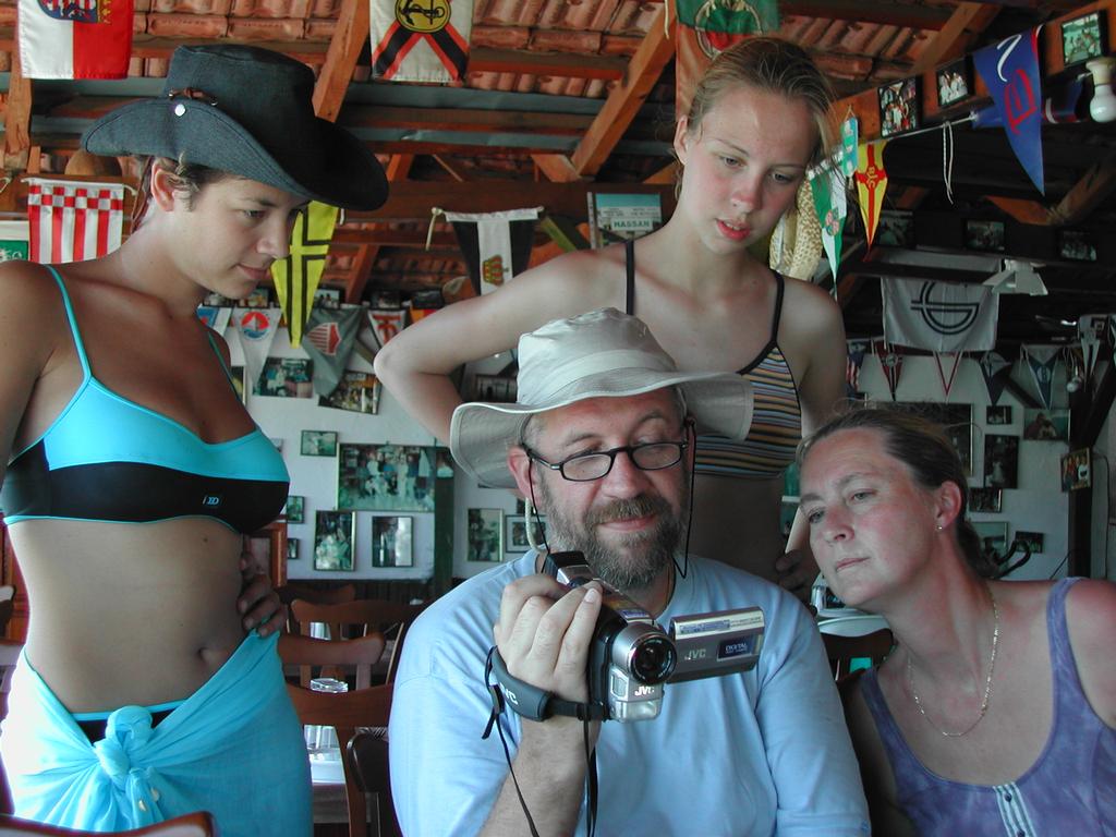 A man in a hat shows a camcorder screen to three women, who are closely watching the footage.