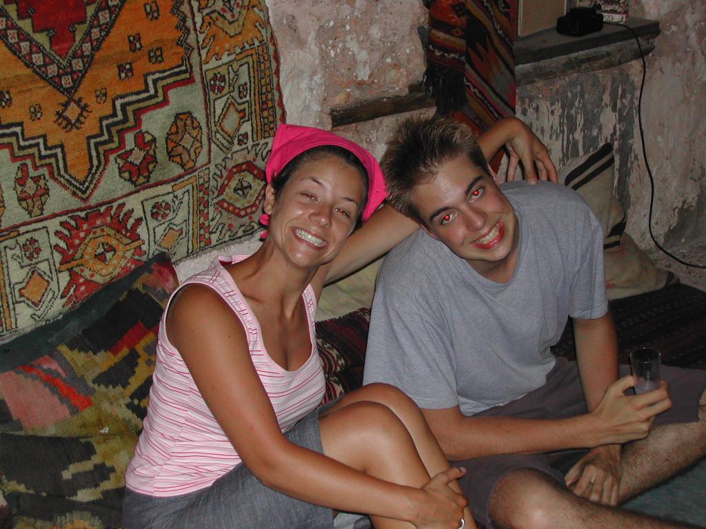 Two people sitting closely on cushions, smiling at the camera.