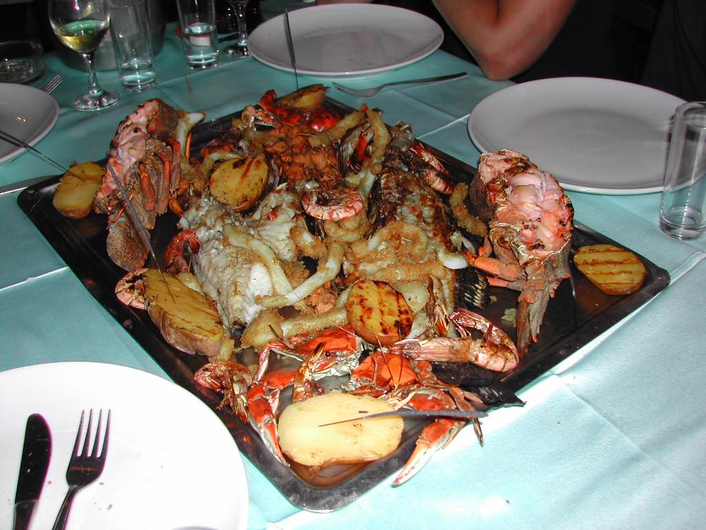 A large seafood platter with grilled fish, crab, lobster, and potatoes on a table set for a meal.