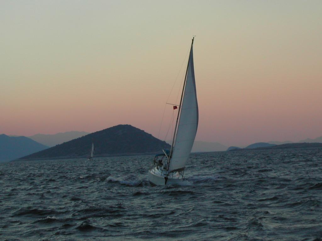 A sailboat moves through choppy waters at sunset, with a small flag on its mast.
