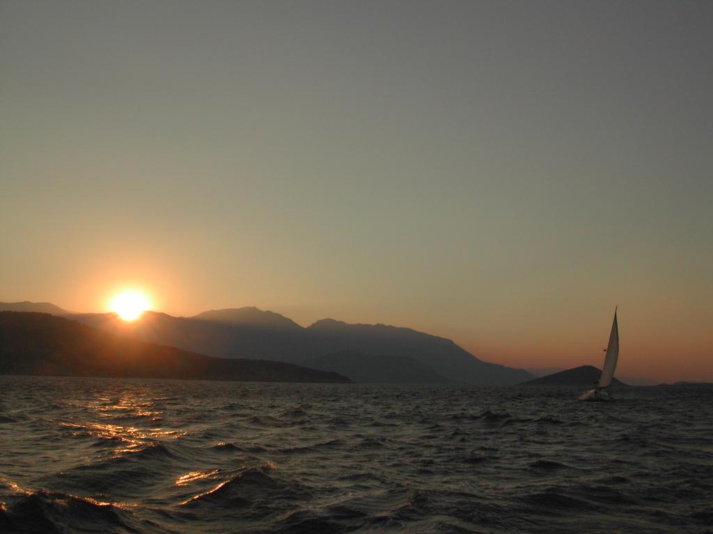 A sailboat moves across the water at sunset, with mountains in the background.