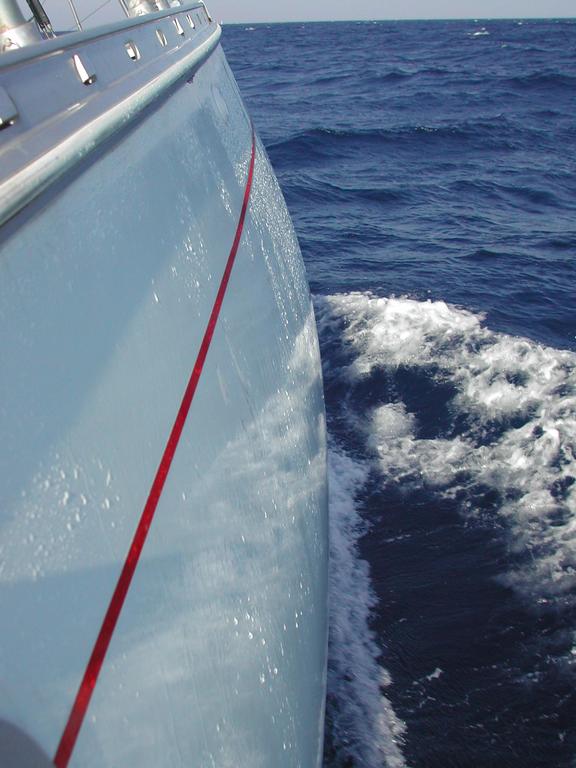 Side view of a boat moving through deep blue water, creating white waves along its hull.