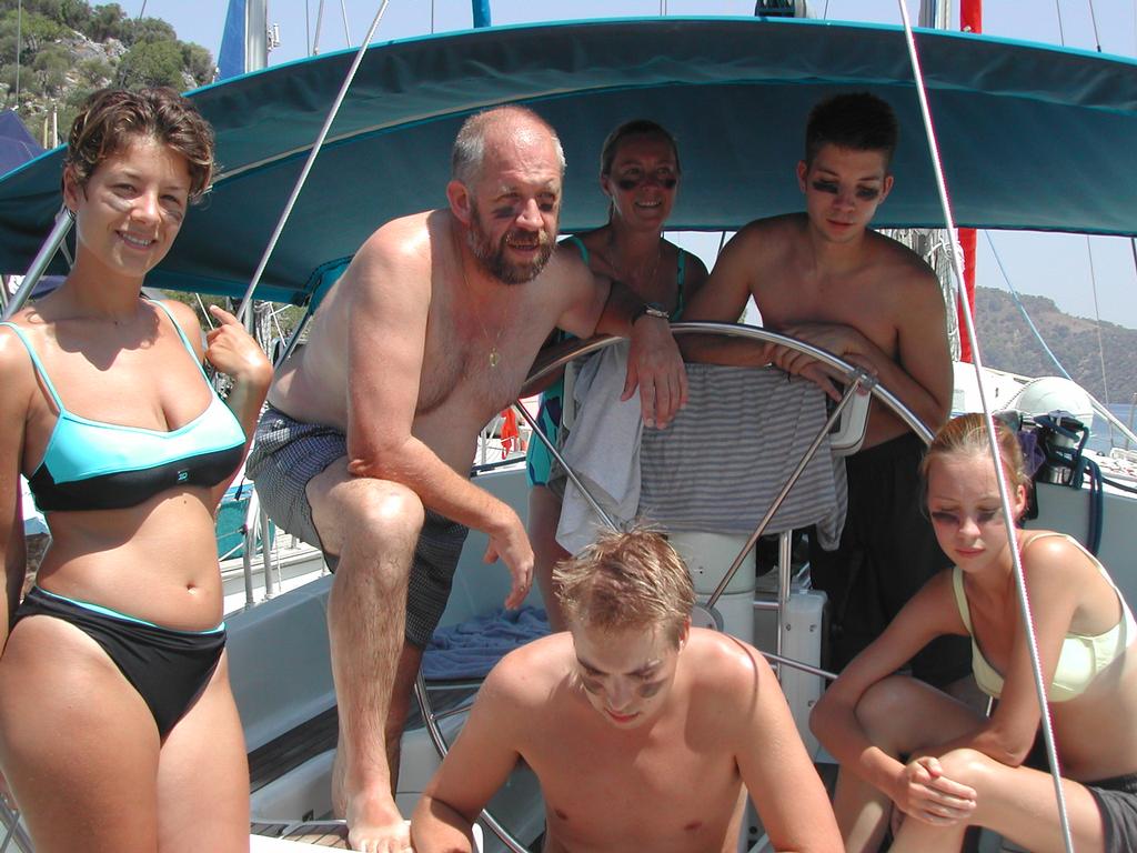 A group of people in swimwear gather on a sailboat, some with face paint, preparing for a regatta.