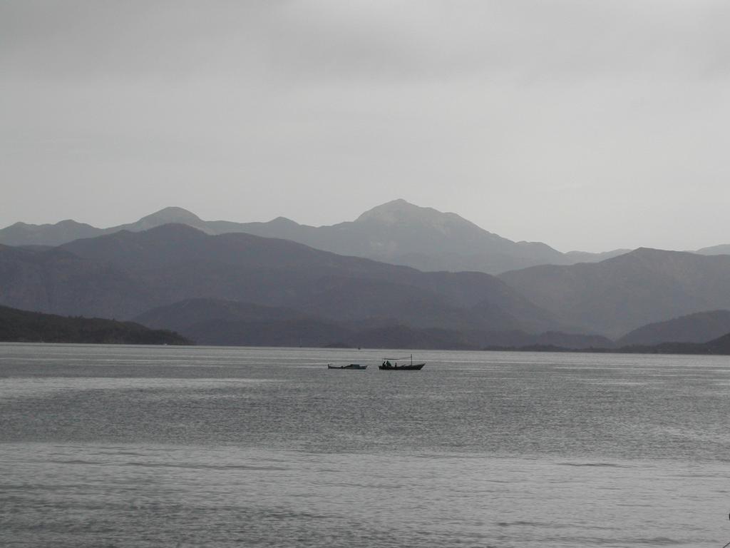 A small boat with people floats on calm water, with distant mountains in the background under a cloudy sky.