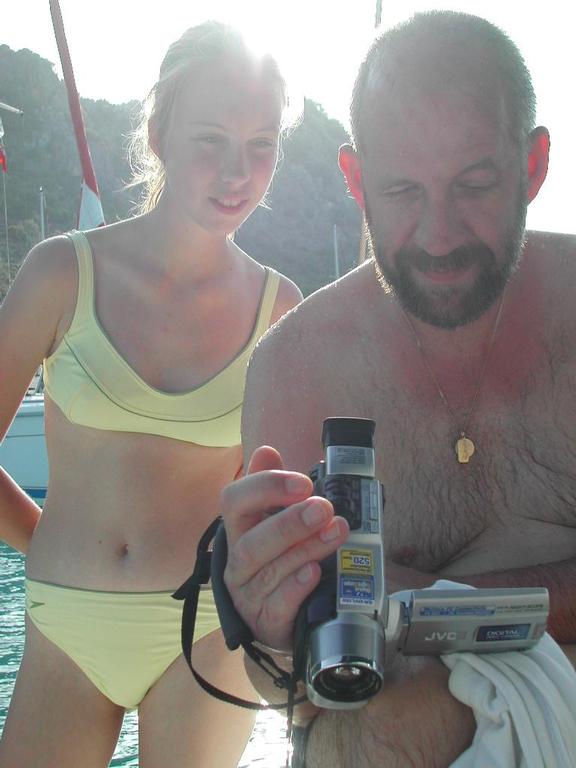 A man and a woman in swimwear review footage on a handheld camcorder near the water.