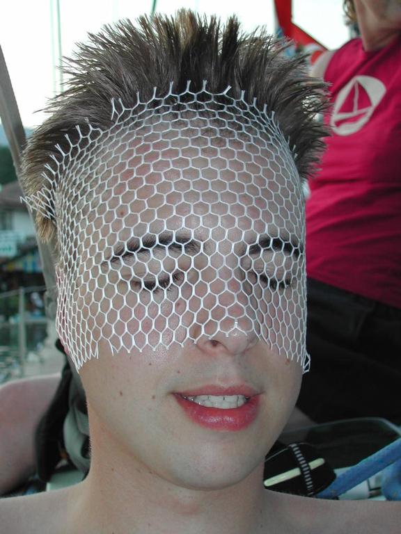 A person with short, spiky hair has a white mesh net covering their face, with eyes closed and mouth slightly open.