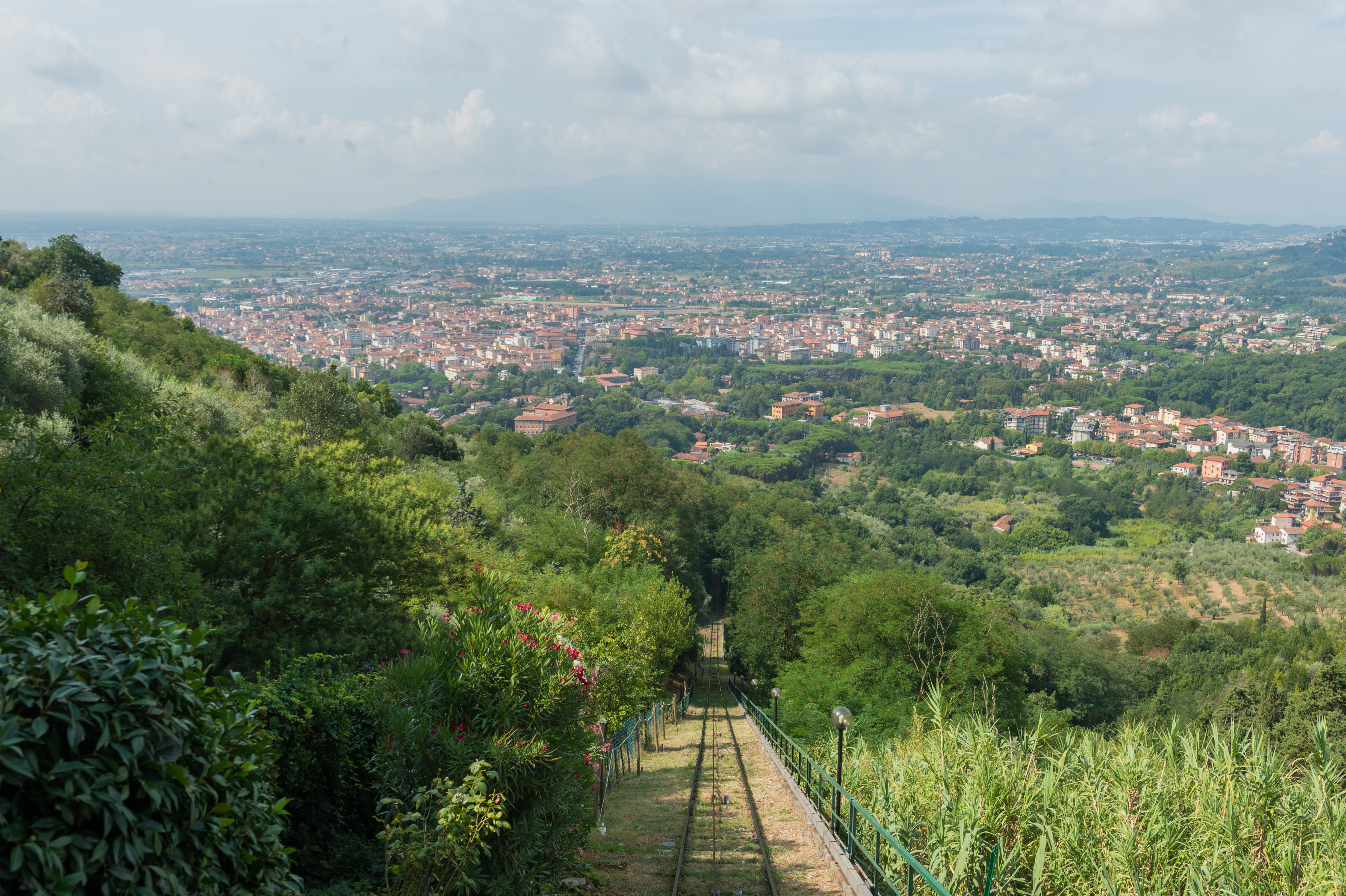Funicular railway tracks descend through green hills, overlooking a cityscape in Montecatini Alto, Tuscany.