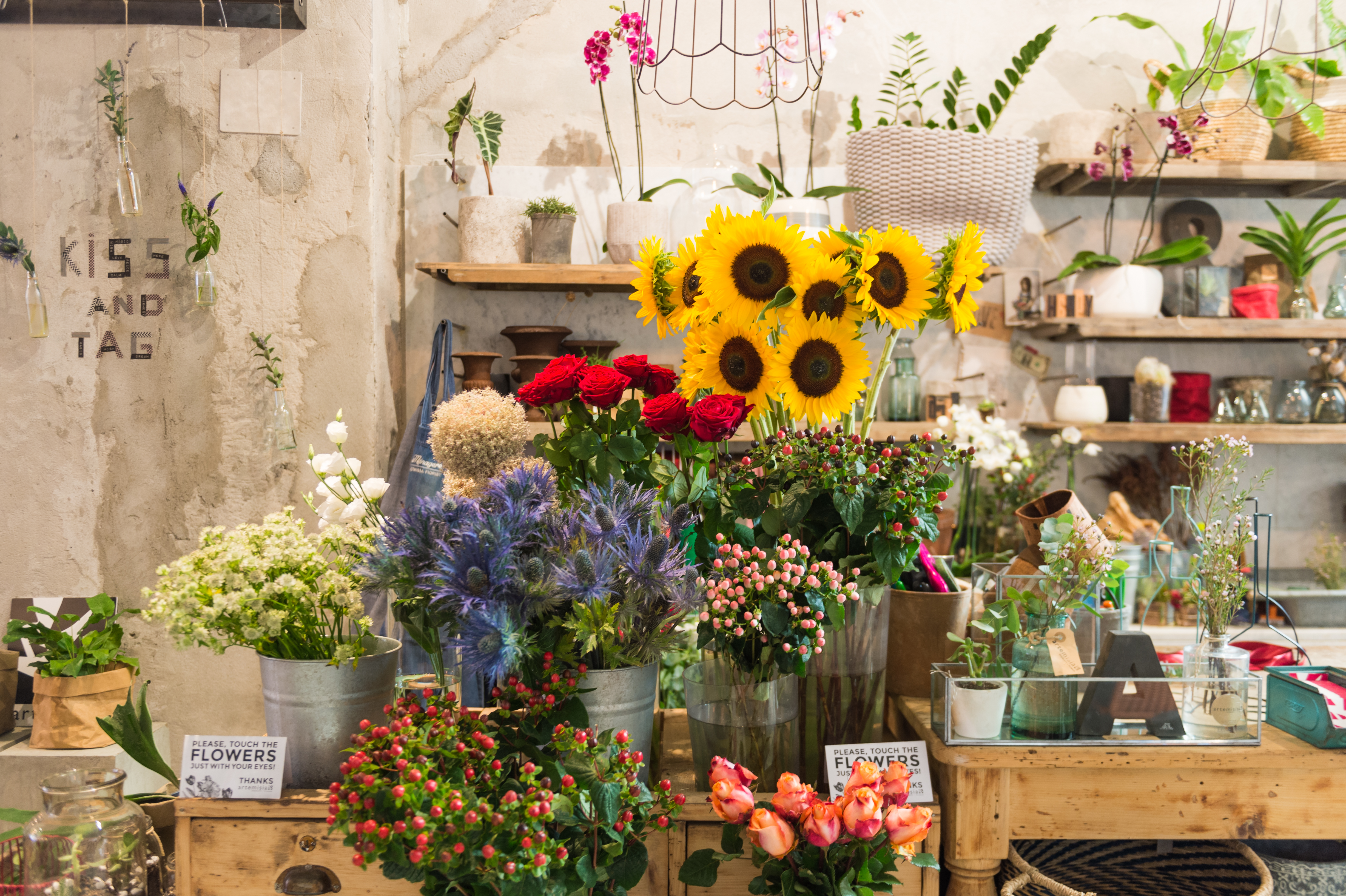 A flower shop display with colorful bouquets, including sunflowers, roses, and wildflowers, arranged in metal buckets.