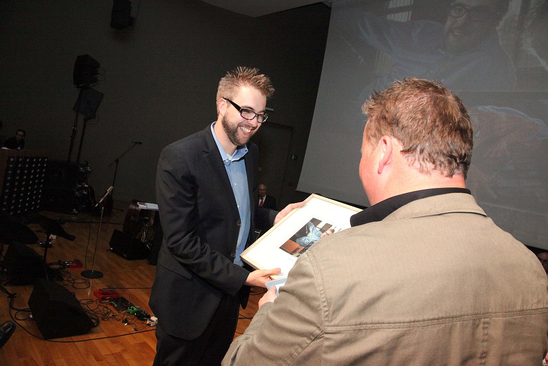 A man in a suit receives a framed award from another person during an alumni event.