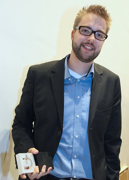 A man in a suit holds an award and smiles at the camera.