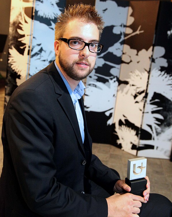 A man in a suit holds an award, recognized as the Alumnus of the Year.