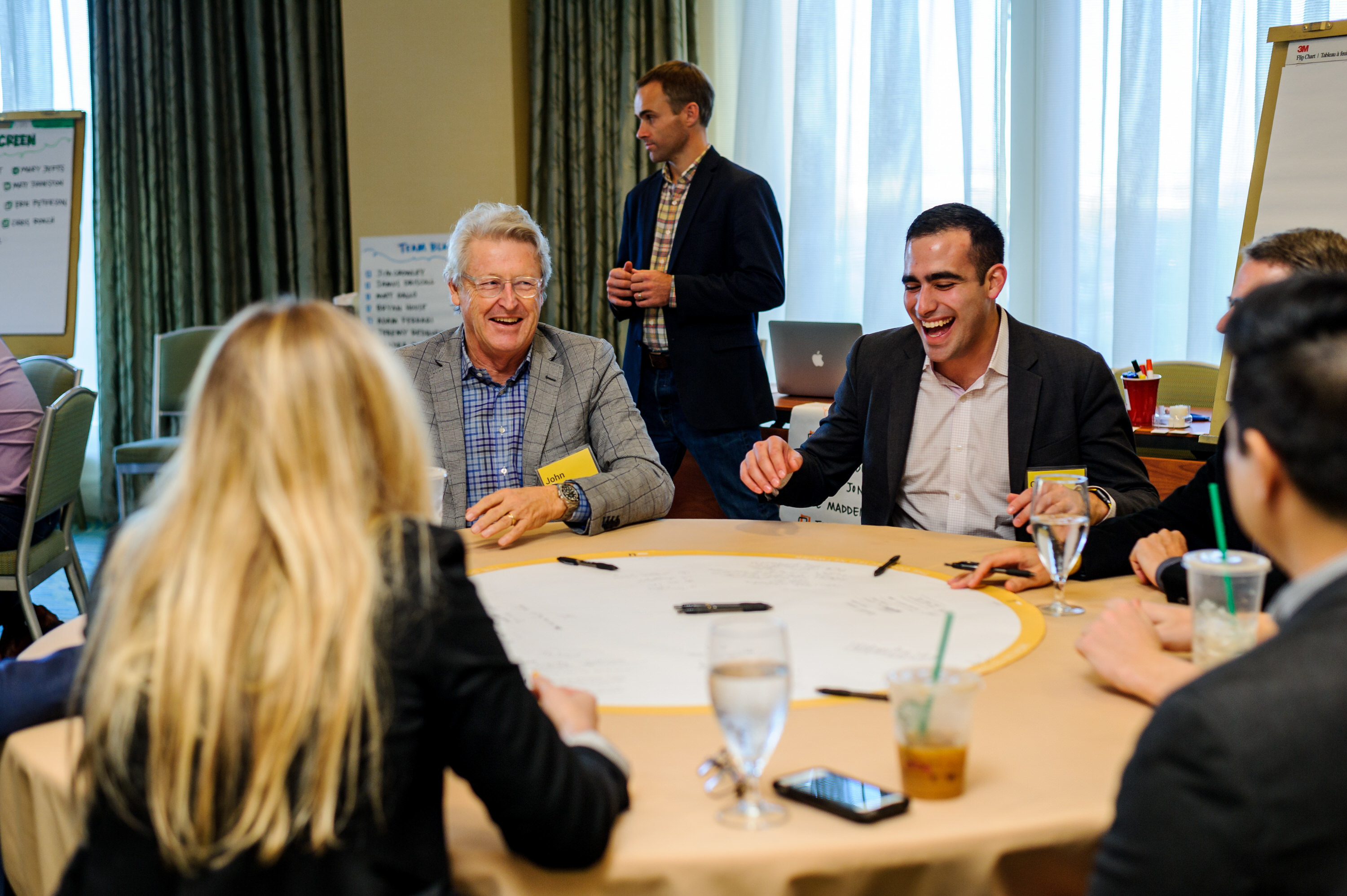 A group of people sits around a table, smiling and discussing during a workshop session.