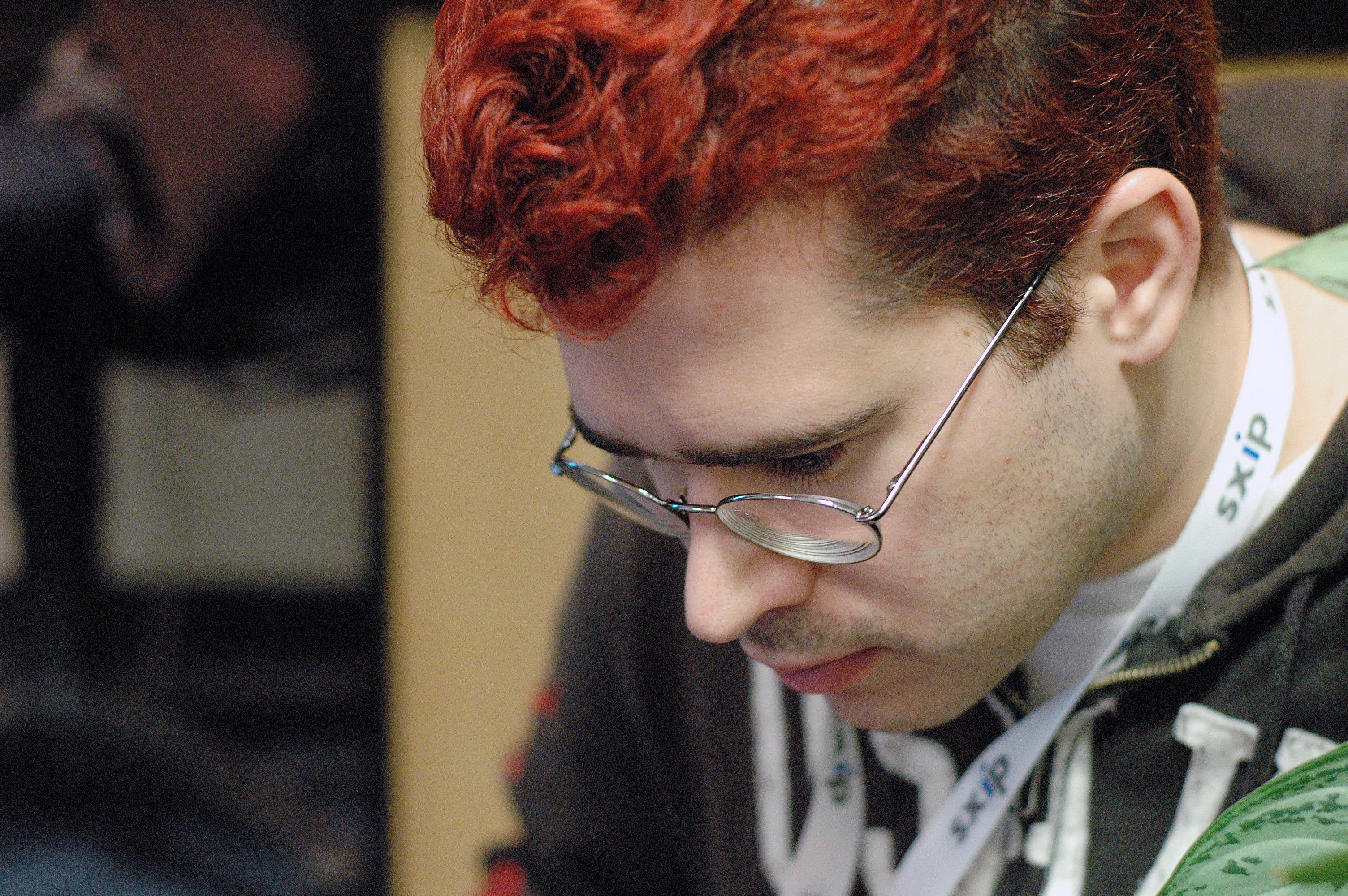 A person with red hair and glasses looks down, wearing a lanyard with "sxip" text.
