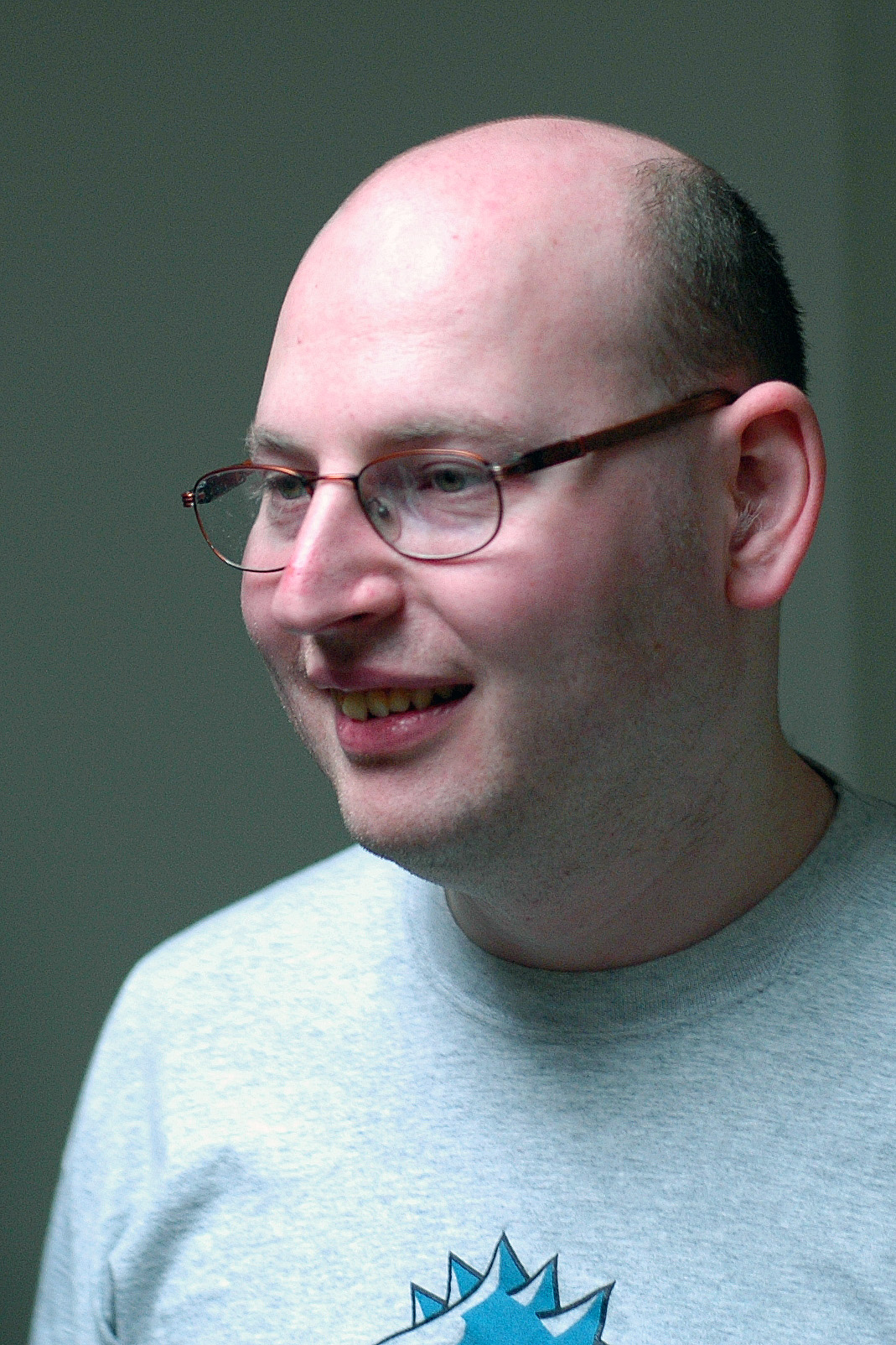 A man wearing glasses and a gray T-shirt smiles while looking to the side.