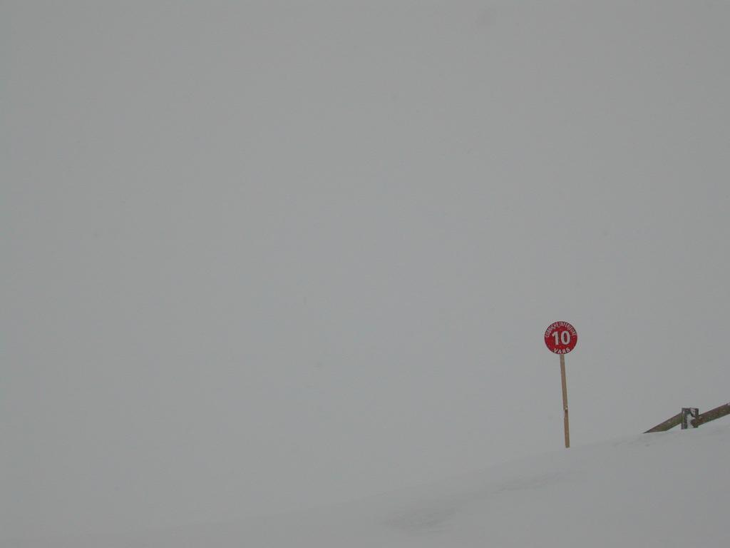 A red ski trail marker with the number 10 stands in a snowy, foggy landscape.
