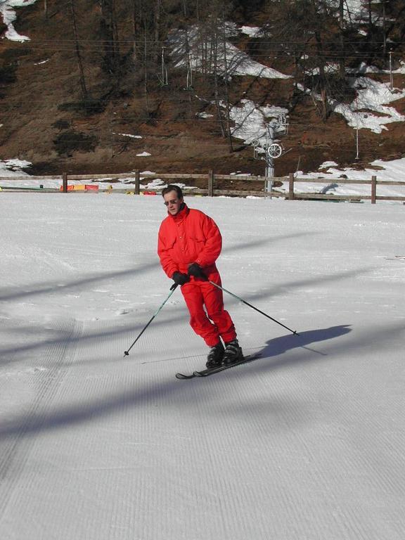 A person in a red ski outfit is skiing on a groomed slope, using ski poles for balance.