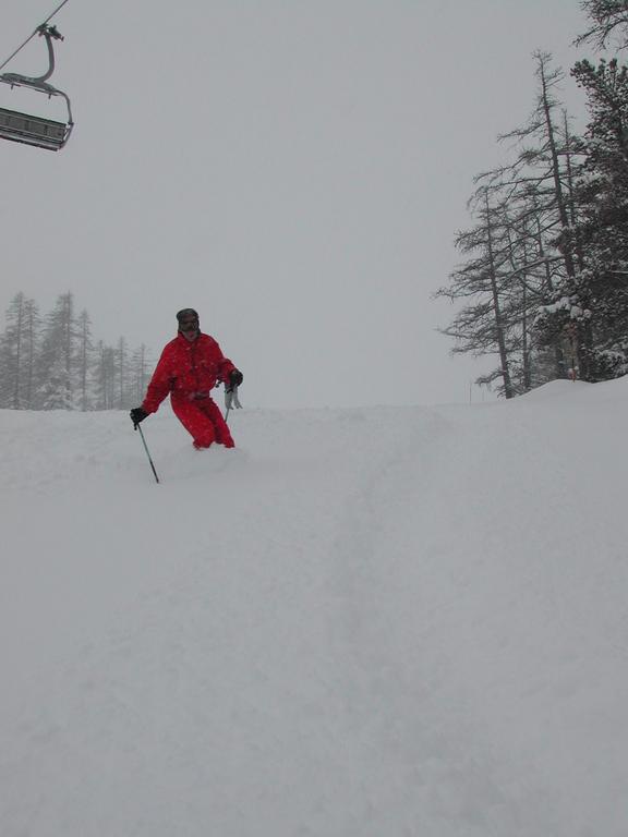 A skier in a red outfit moves downhill through fresh snow, using ski poles for balance.