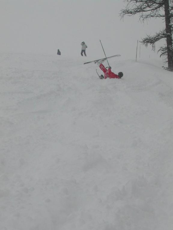 A skier in red has fallen in the snow, with skis and poles scattered around them.