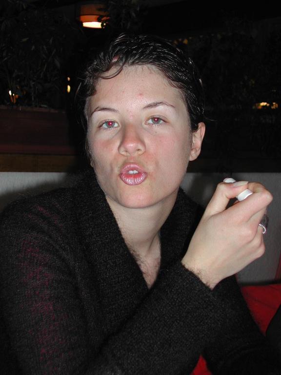 A person with short, wet hair holds a spoon and makes a playful expression while sitting indoors.