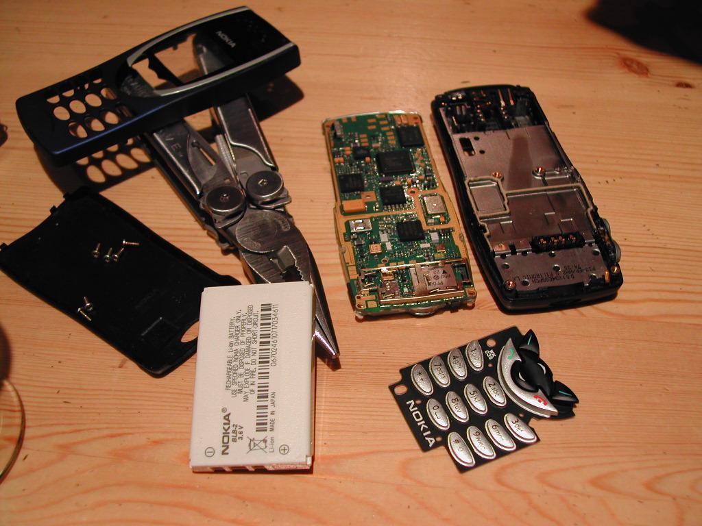 A disassembled Nokia mobile phone with its battery, keypad, circuit board, and casing spread out on a wooden surface.