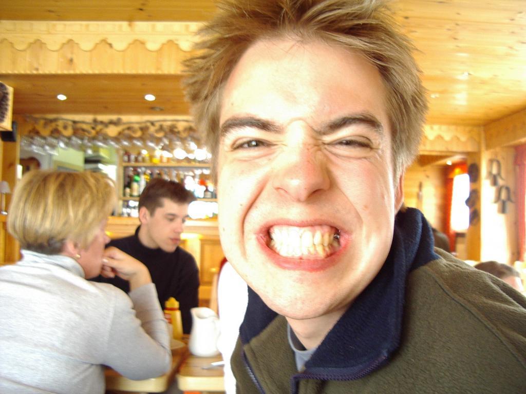A person in the foreground grins widely at the camera, showing their teeth.